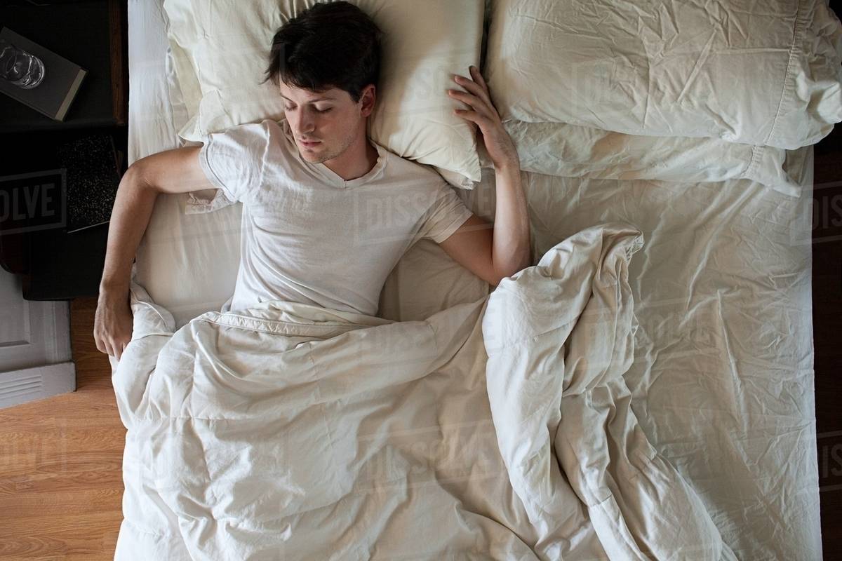 Man sleeping alone in double bed Stock Photo Dissolve