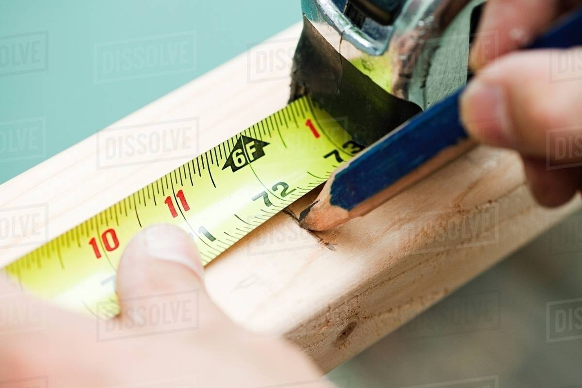 Woman measuring plank of wood and marking with pencil Stock Photo