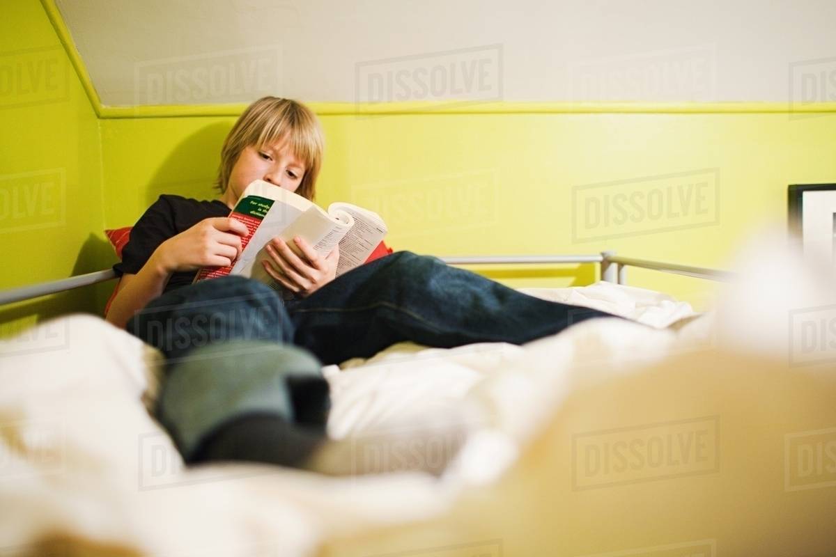 Boy reading book on bed Stock Photo Dissolve