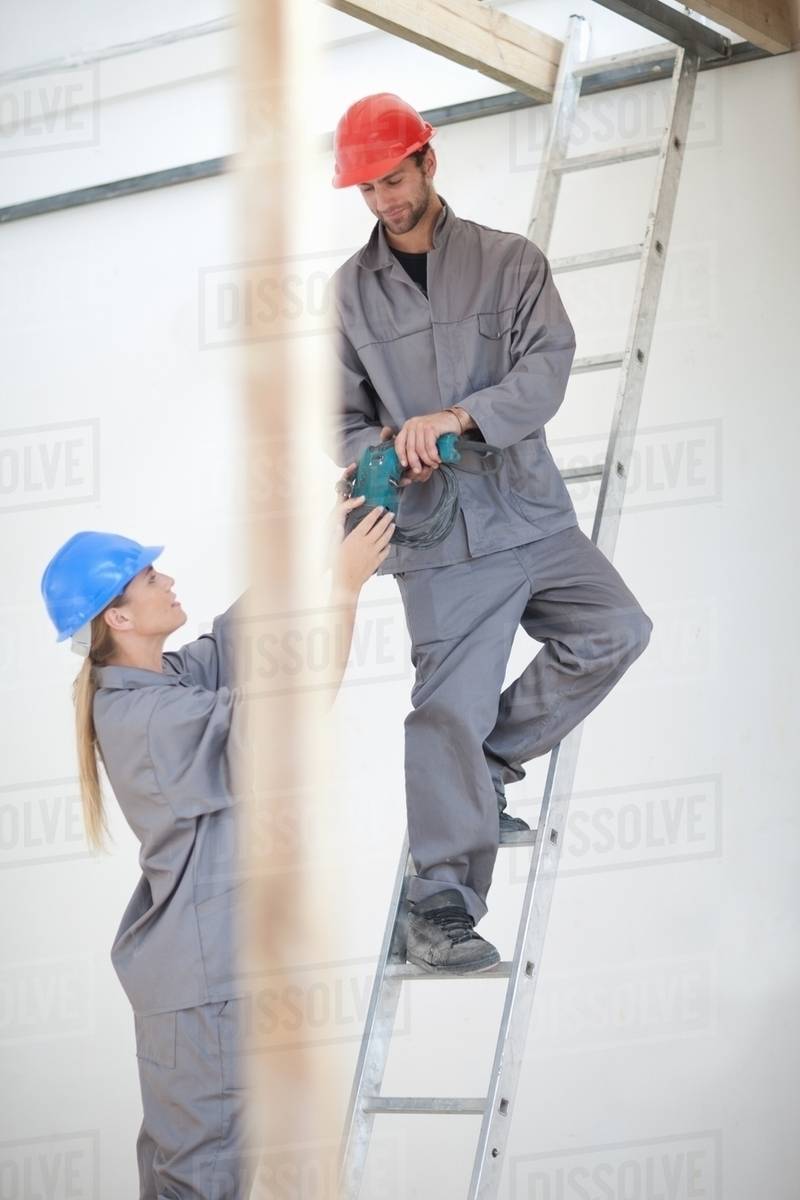 Male and female laborer with electric drill on construction site ...