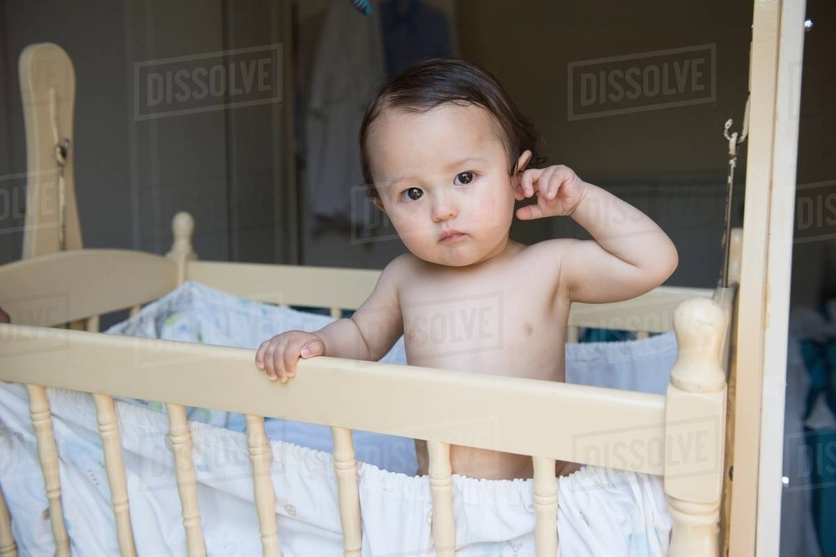 Portrait of tired baby boy standing in crib Stock Photo Dissolve