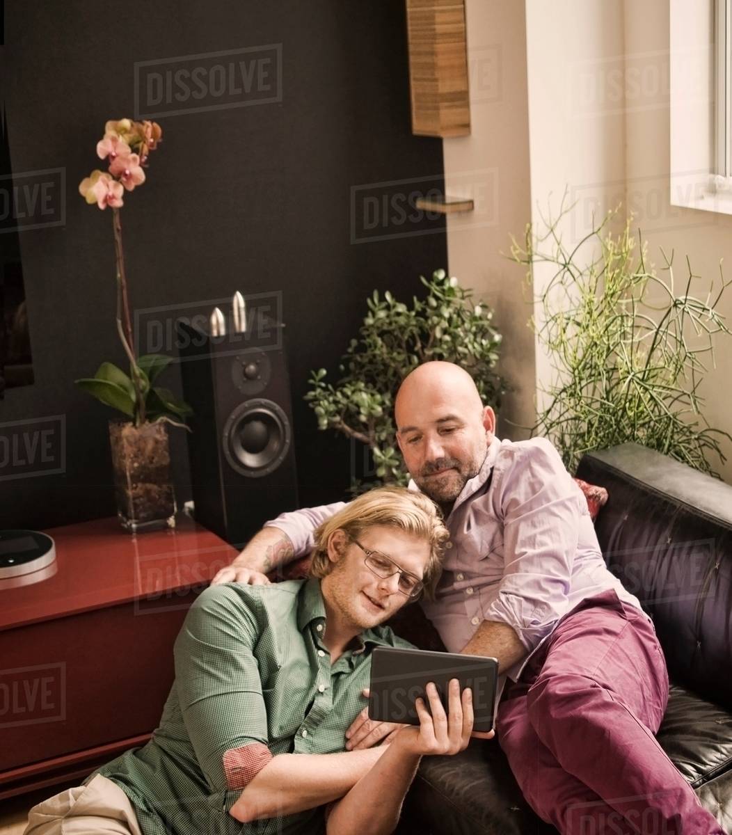 Male couple reclining on sofa looking at digital tablet Stock Photo