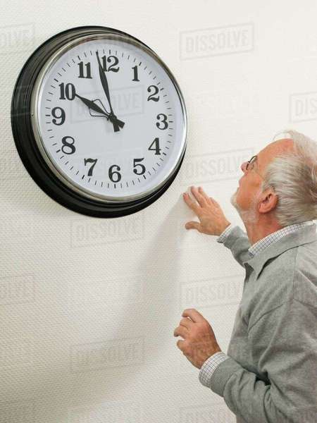 Senior man looking at a large clock - Stock Photo - Dissolve