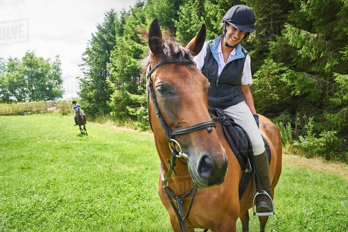 Mature woman on horseback wearing riding hat and boots looking at horse