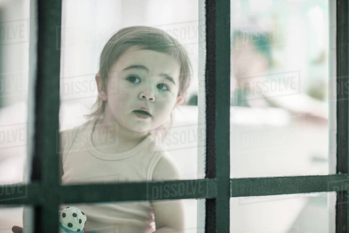 Baby girl looking through window Stock Photo Dissolve