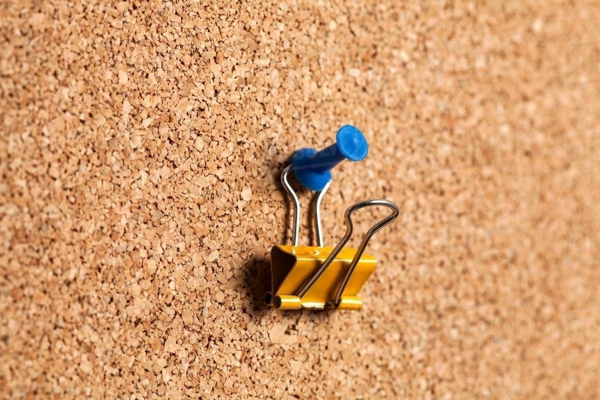 Bulldog clip hanging on corkboard Stock Photo Dissolve