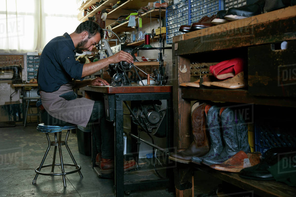 Male cobbler in traditional shoe at sewing machine Stock