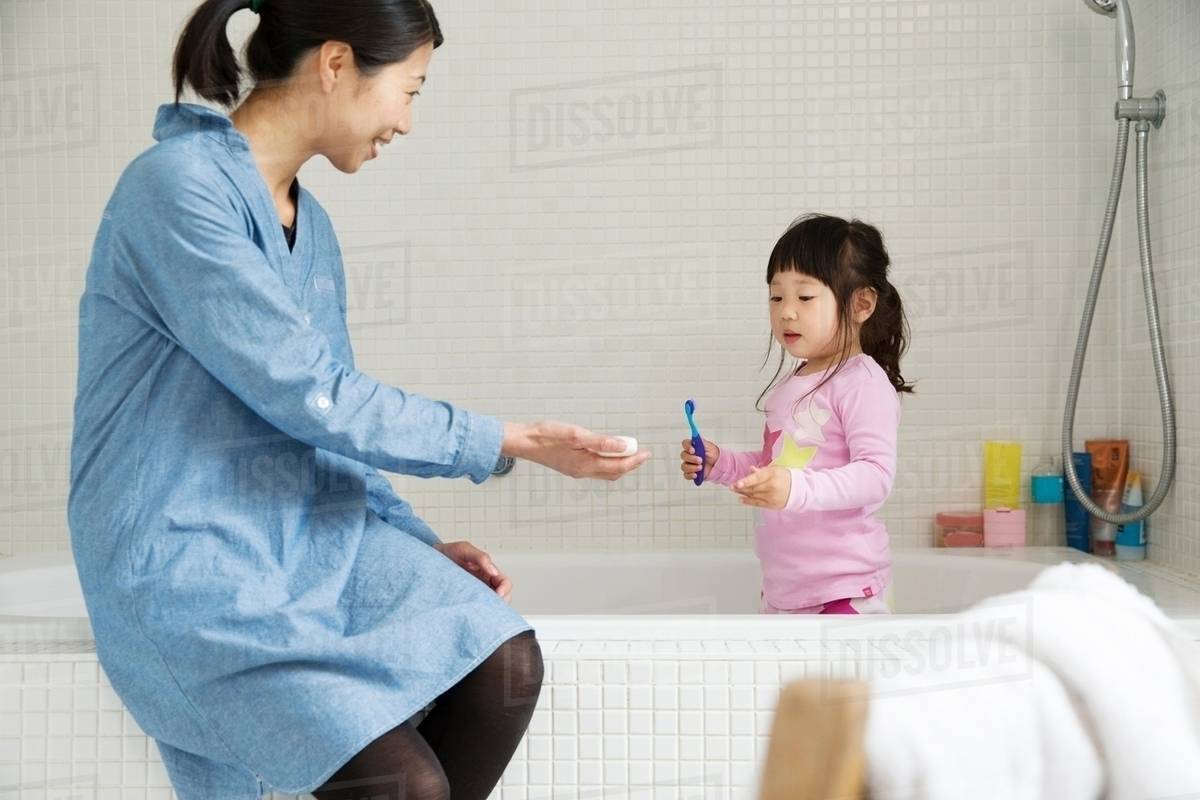 Mother with female toddler standing in bath with tooth brush Stock