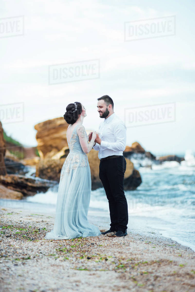 same couple with a bride in a blue dress walk along the ocean shore -  Royalty-free Stock Photo | Dissolve