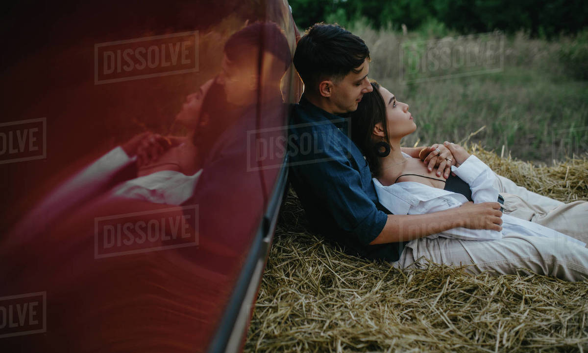 Young couple in love rests on haystack near red car on meadow. Royalty-free stock photo