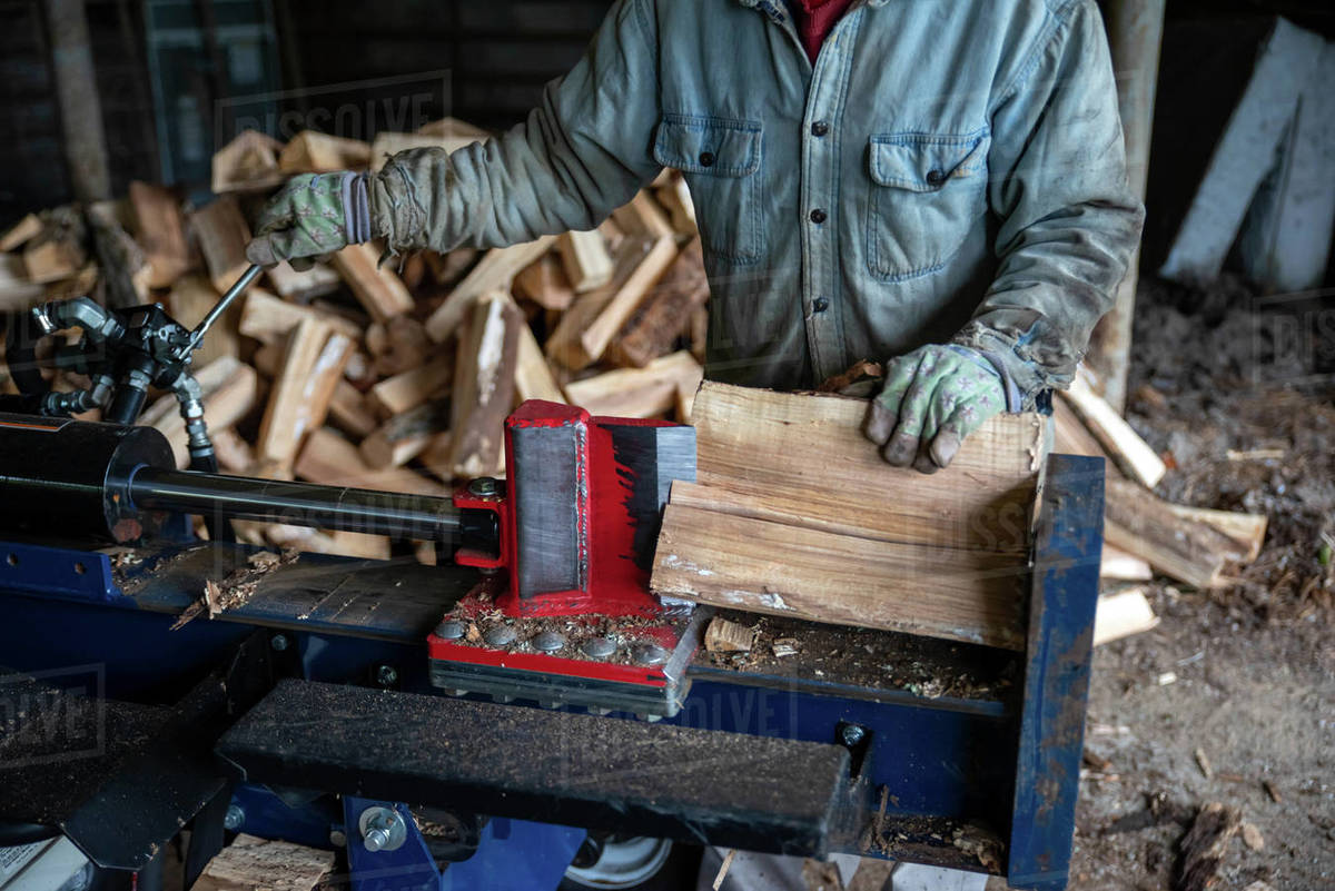 Work man splits wood with a hydraulic log splitter. Blade is seen