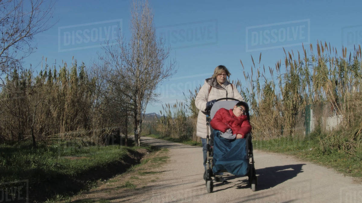Woman wheelchair pass disabled child on a dirt road. Stock Photo