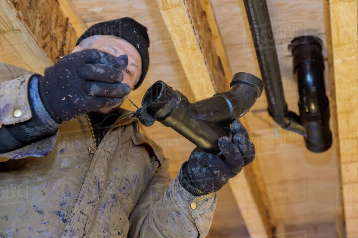 Plumber hands in glue pieces of plastic drains PVC pipe, close up on