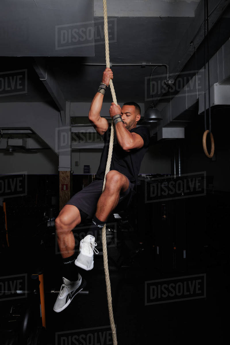 a latin american adult is climbing a rope at the gym with a great