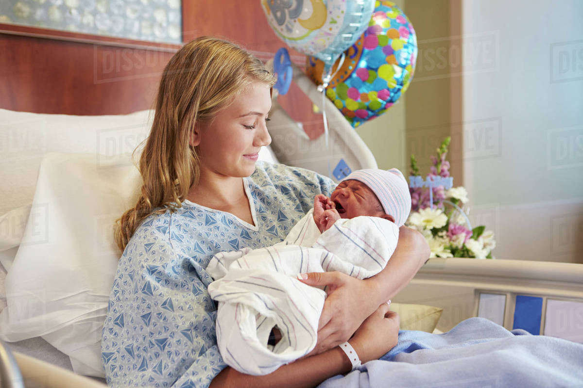 Teenage girl holding newborn baby son in hospital Stock Photo Dissolve