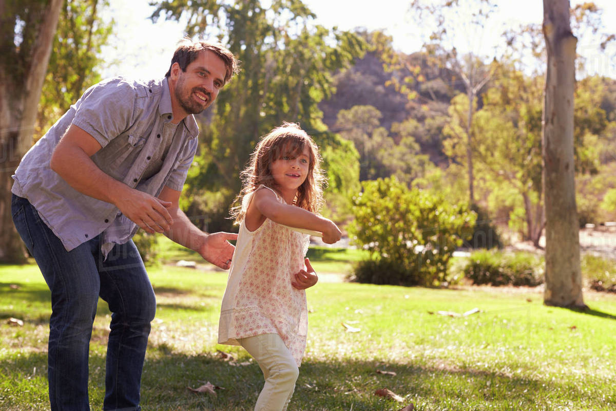 Father teaching daughter to throw frisbee in park Stock Photo Dissolve