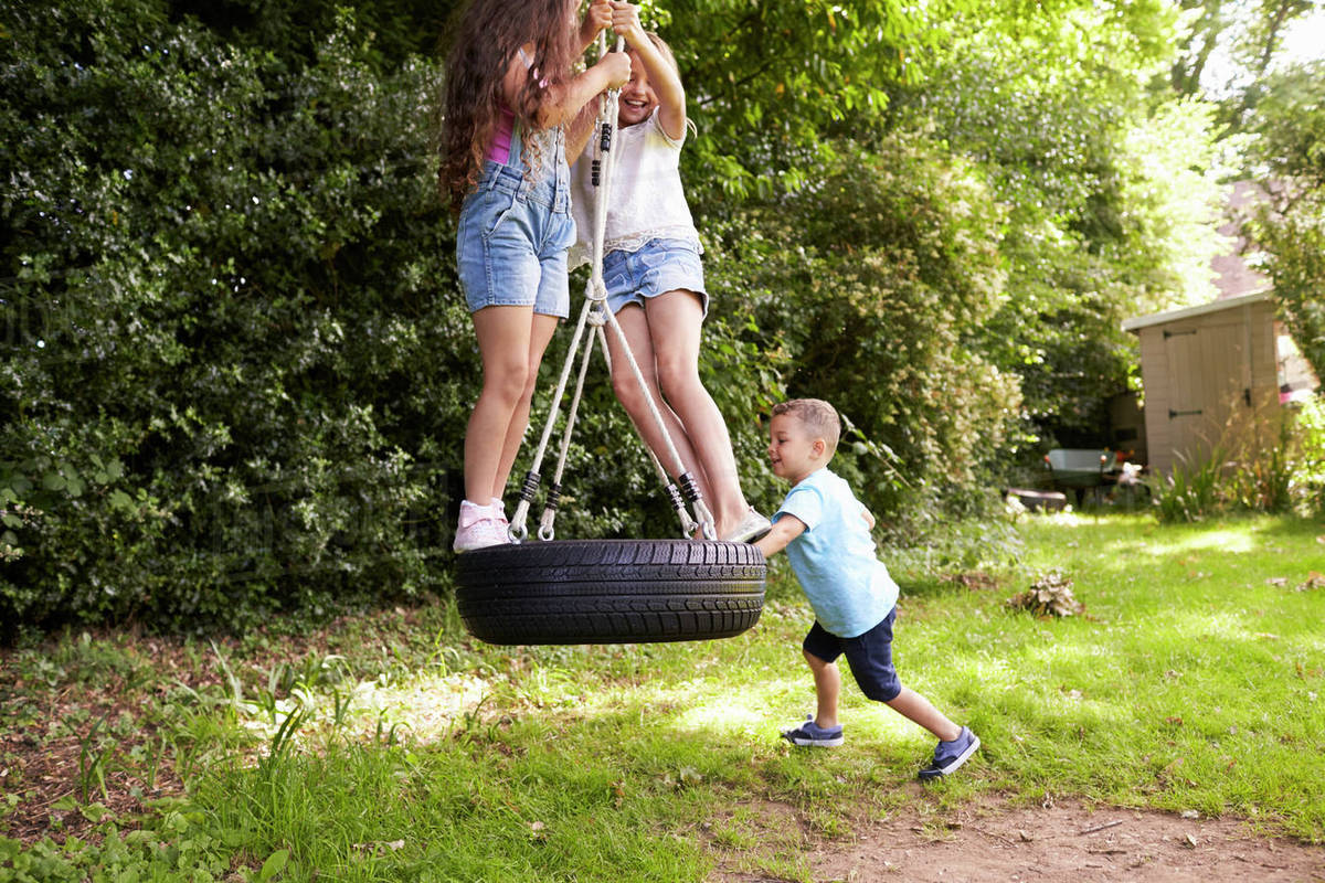 Group of children playing on tire swing in garden Royalty-free