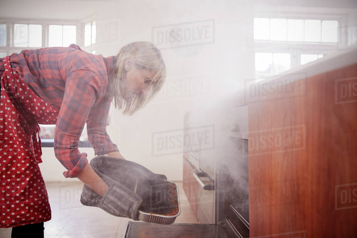 Middle aged woman opening smoke filled oven in the kitchen Stock