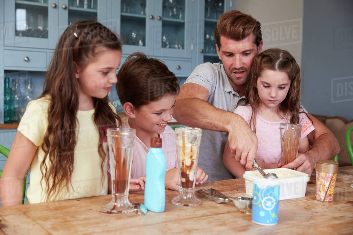 Father Making Ice Cream Sundaes With Children At Home Stock Photo