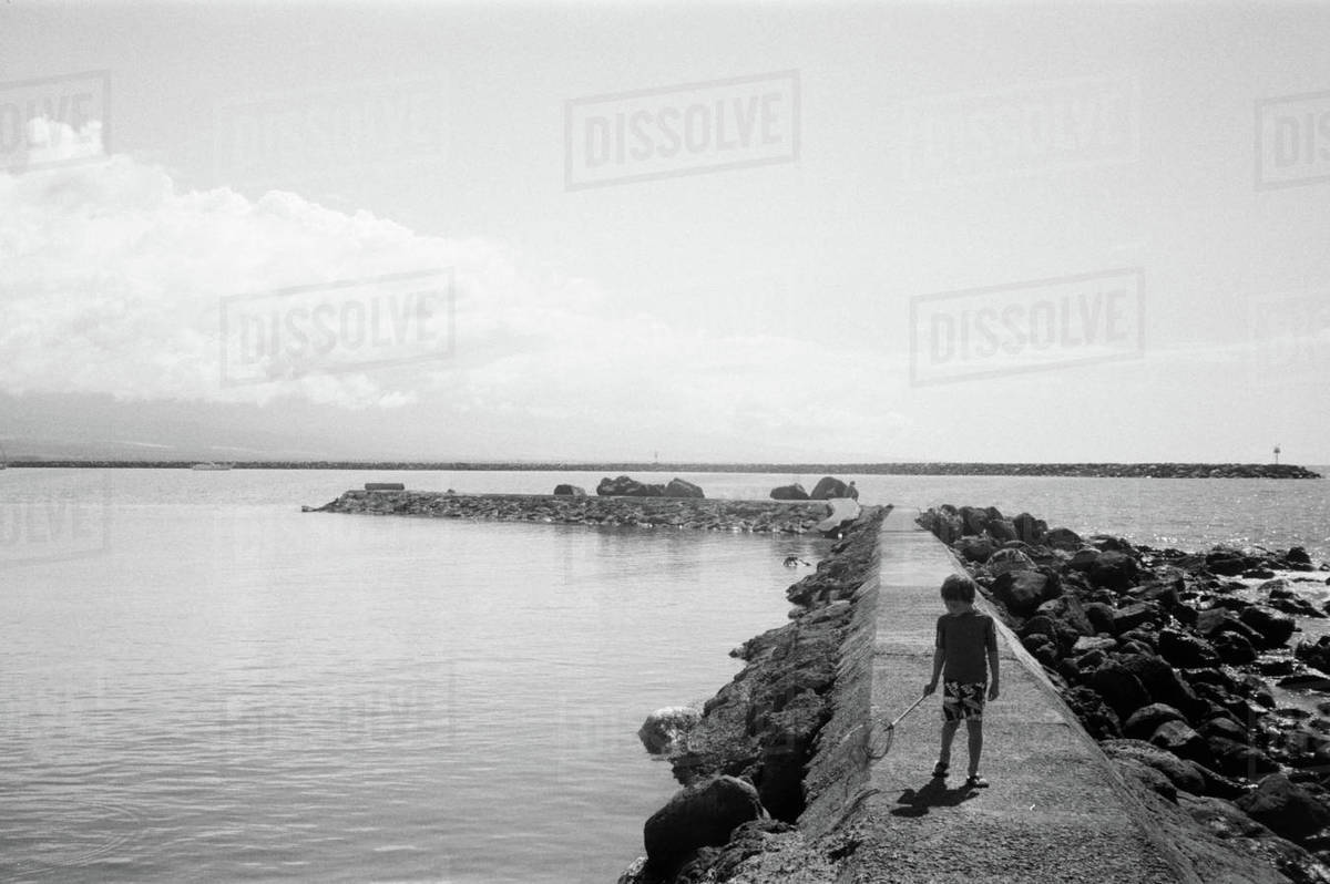 Boy with fishing net walking on seawall at Kawaihae Harbor, Hawaii, United States of America