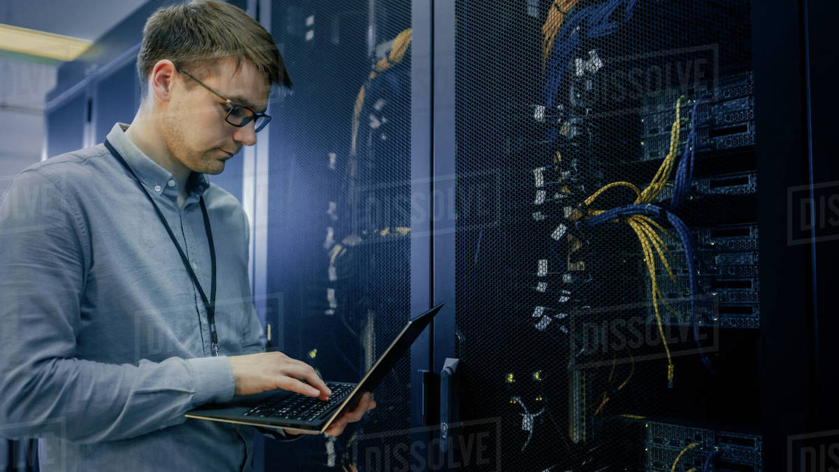 In Data Center IT Engineer Stands Before Working Server Rack Doing