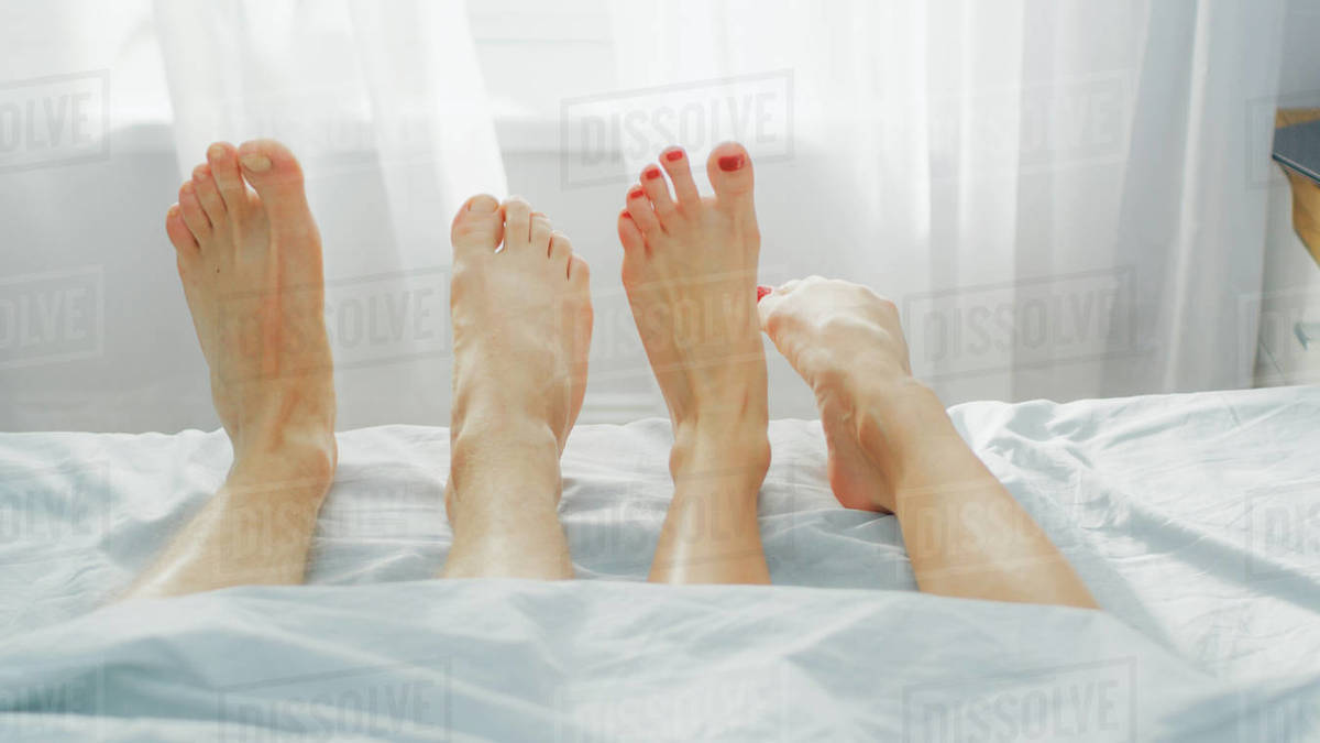 Cute Male and Female Lying in Bed with Legs Sticking from Under the