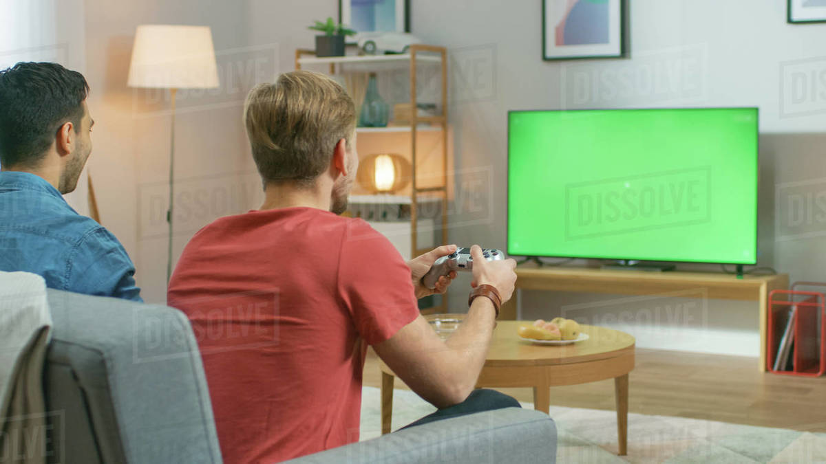 In the Living Room Two Friends Sitting on a Couch Holding Controllers