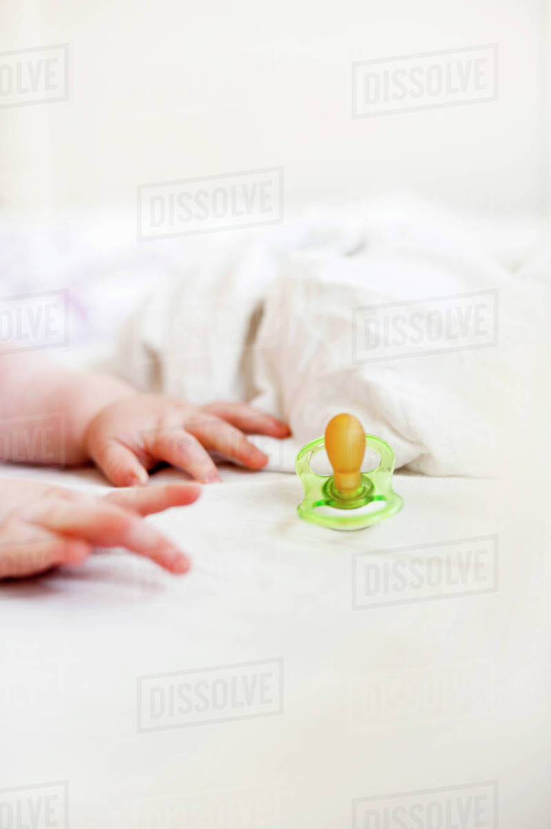Pacifier and babys hands on bed Stock Photo Dissolve