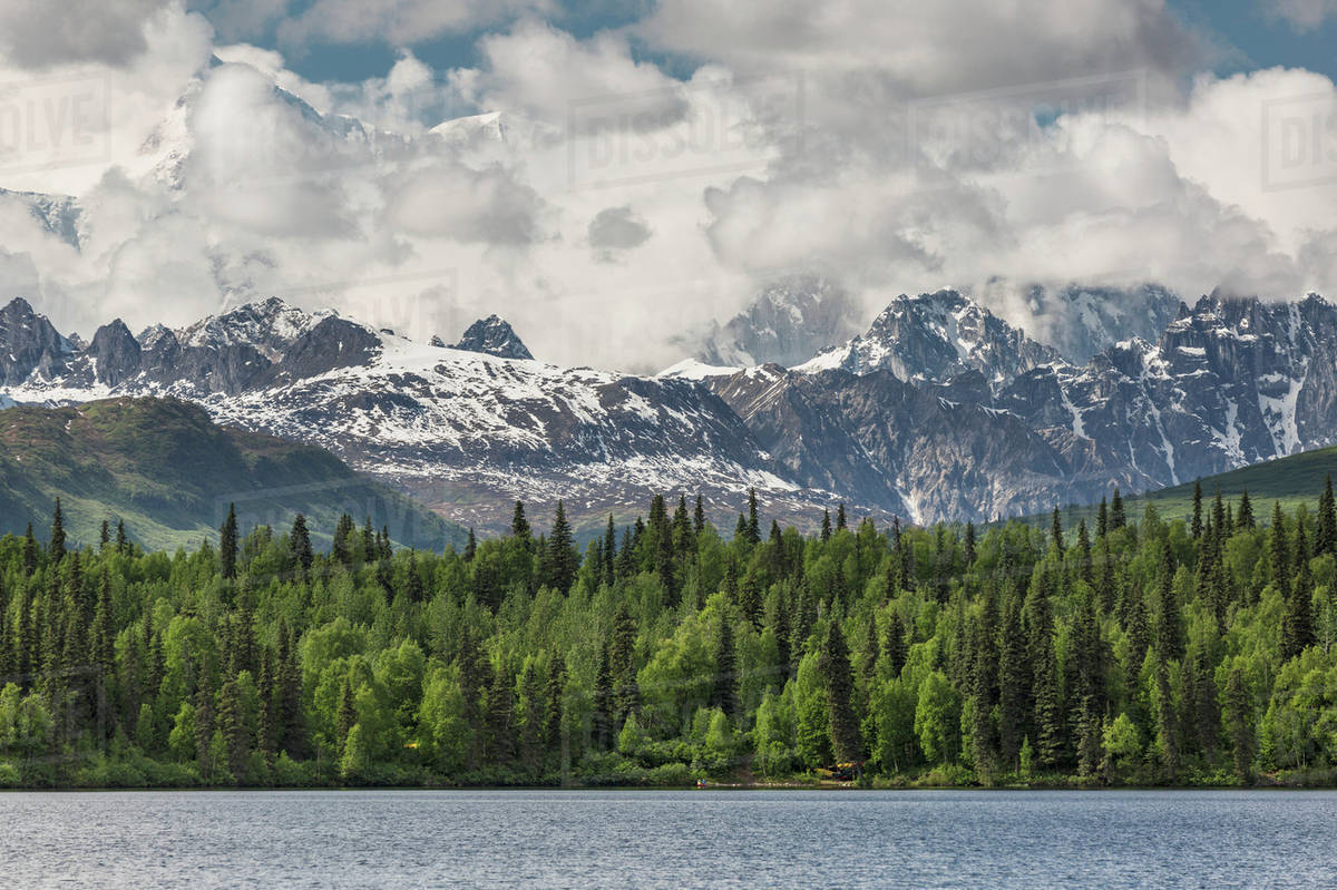 Mt McKinley peaking through the clouds behind snowy rocky foothills of