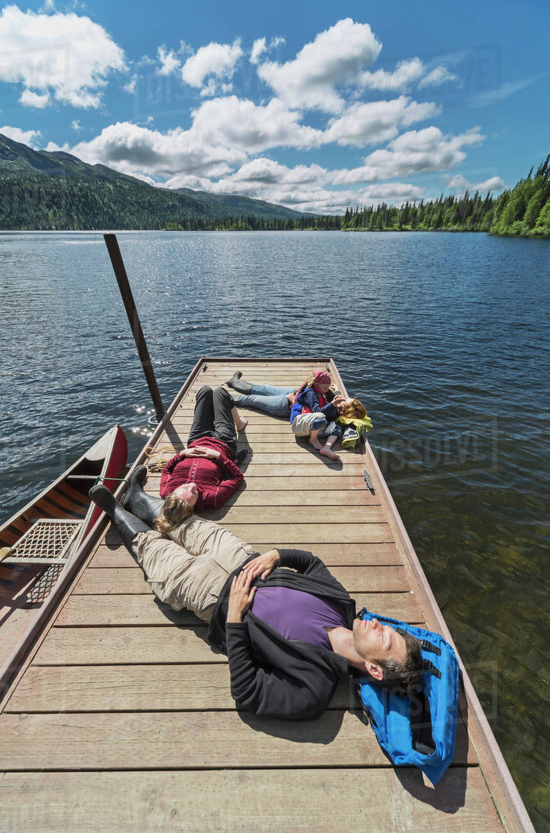 Three adults and a young girl lounging on a boat dock on a lake soaking