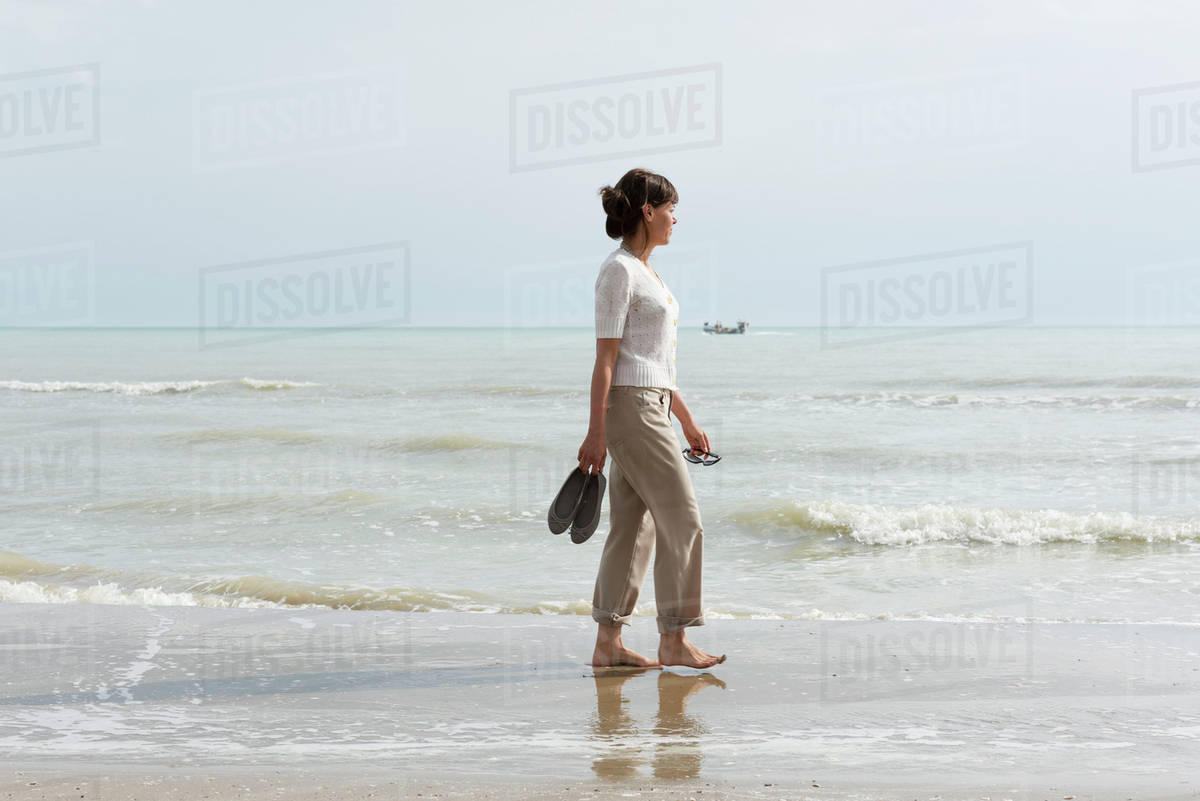 A Woman Walking On The Wet Beach Carrying Her Shoes D869 28 015 A Woman Walking On The Wet Beach Carrying Her Shoes D869 28 015