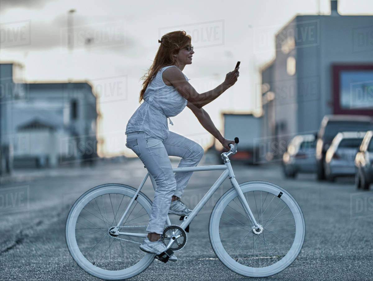 A Woman Riding Her Bike And Using Her Cell Phone While Crossing