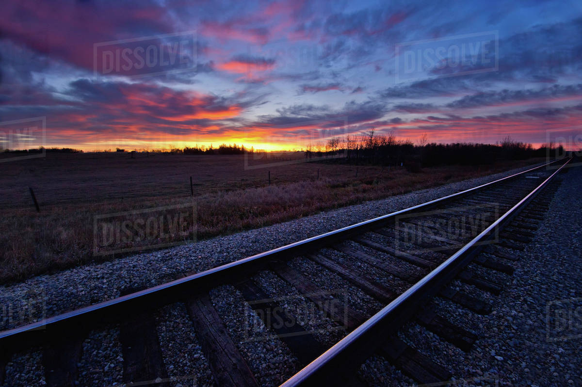 Train tracks and a dramatic colourful sky at sunset;Millet alberta