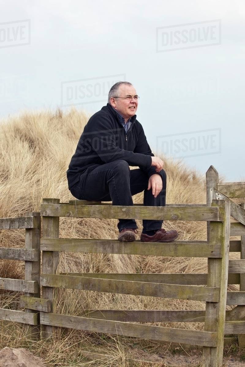 Northumberland, England; A Man Sitting On A Fence Stock Photo Dissolve