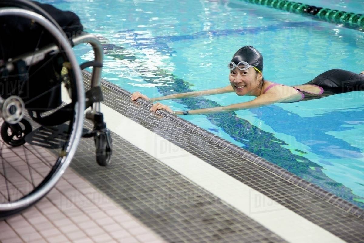 A Paraplegic Woman Swims In A Pool With Her Wheelchair At The Water's