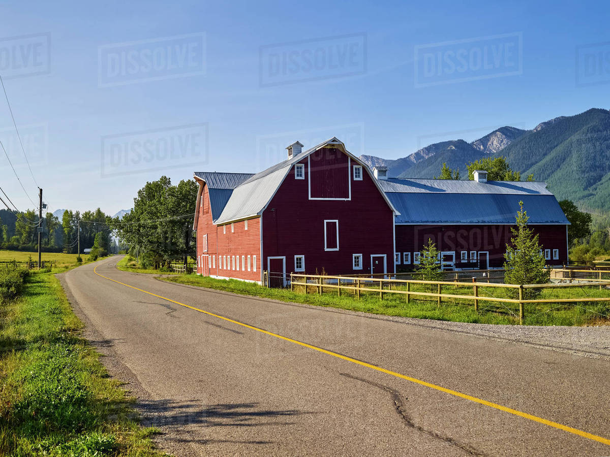 A large red barn beside a country road and a mountain range in the ...