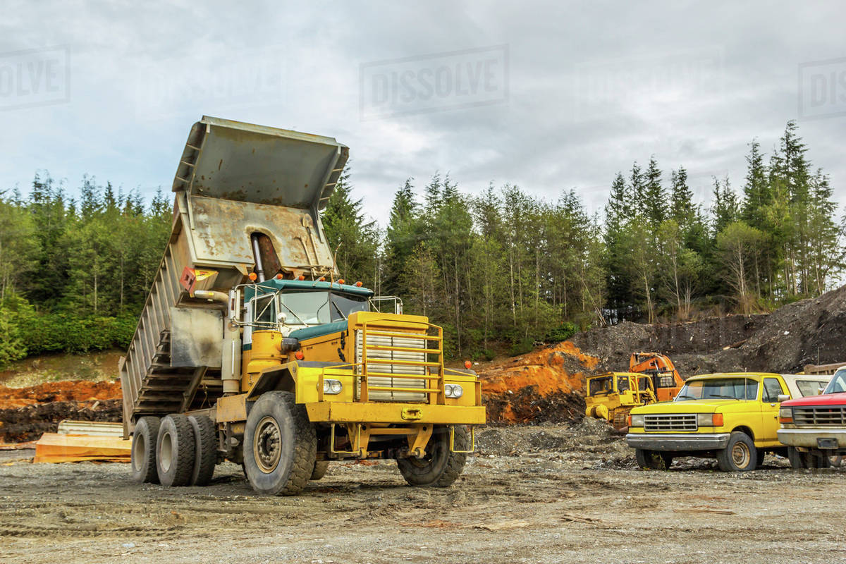 An old dump truck is positioned in a gravel yard with box raised up