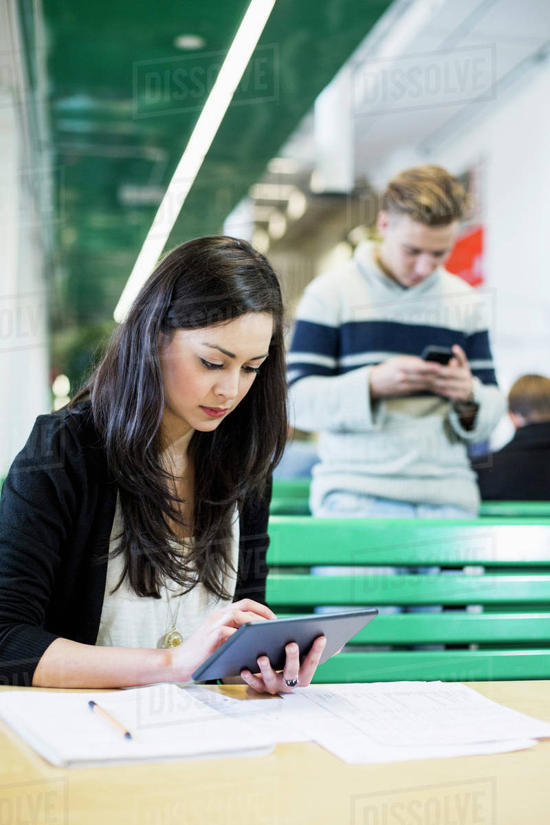 Female university student using digital tablet with friend in background Royalty-free stock photo