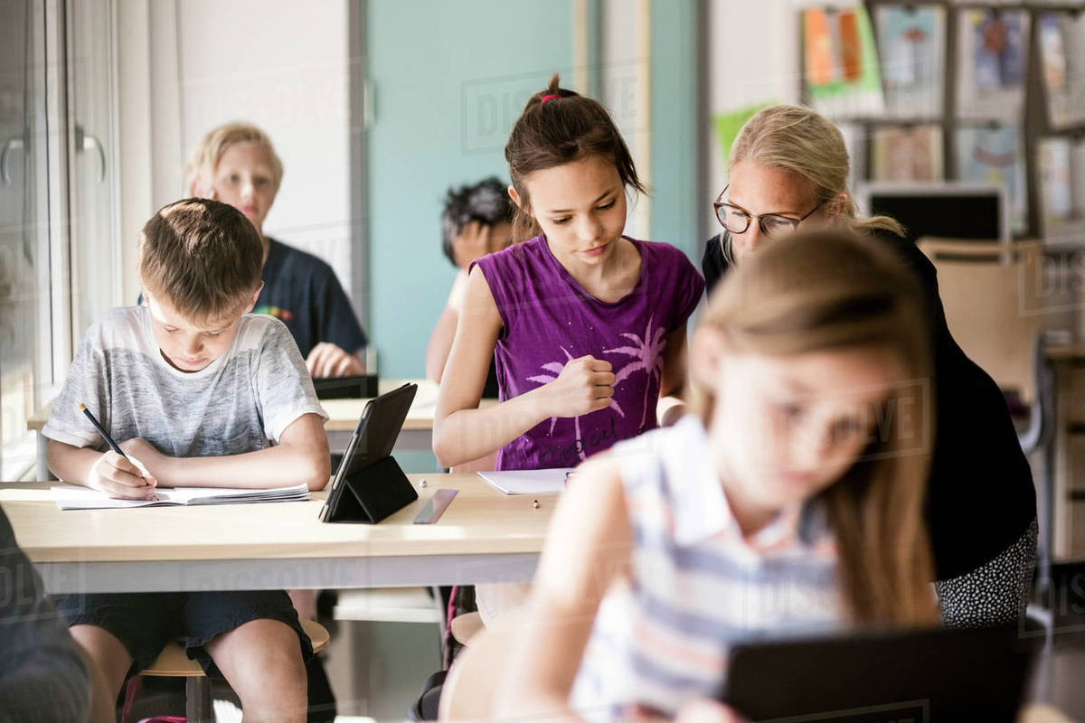 Teacher assisting schoolgirl by boy in classroom Royalty-free stock photo