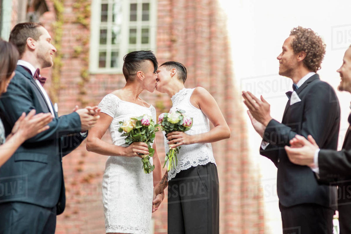 Low angle view of friends clapping while looking at lesbian couple kissing each other Royalty-free stock photo