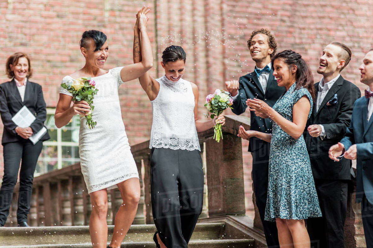 Low angle view of cheerful lesbian couple on staircase with raised hands by friends Royalty-free stock photo