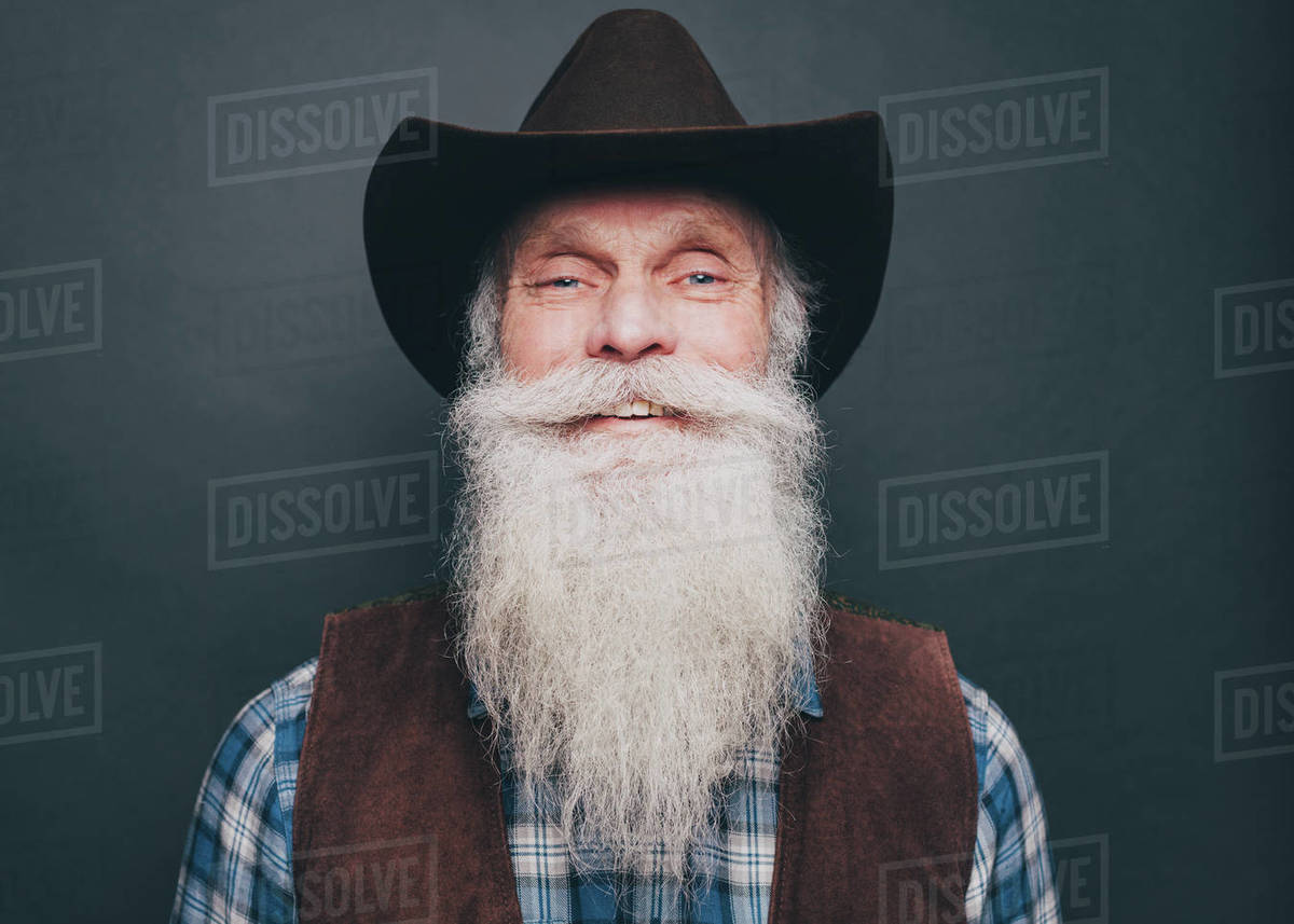 Portrait Of Happy Bearded Senior Man Wearing Cowboy Hat On Gray