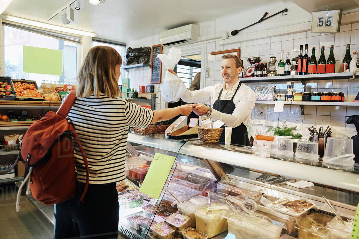 male sales clerk holding plastic bag while accepting credit card d929_50_785 what is a sales clerk