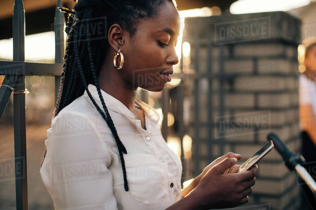 Young woman text messaging through smart phone while standing against fence in city Royalty-free stock photo