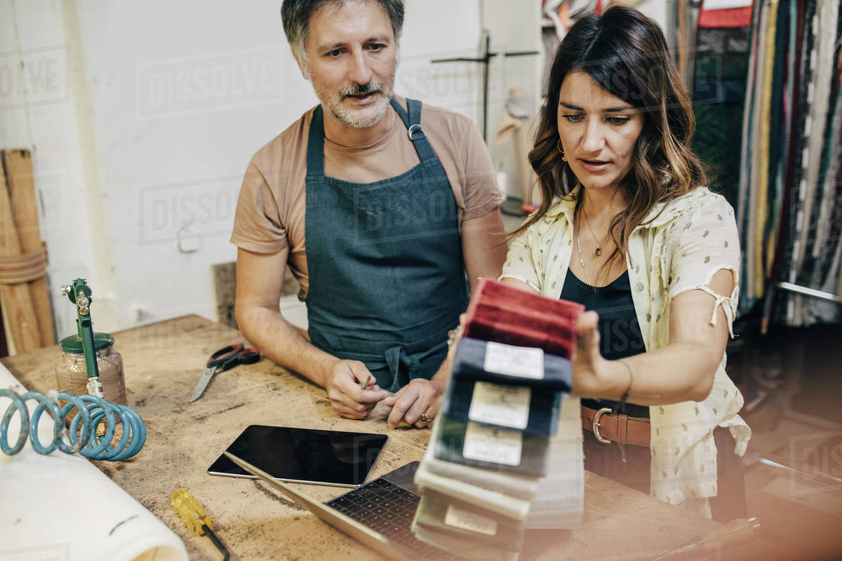 Female upholstery worker explaining male colleague over fabric swatch