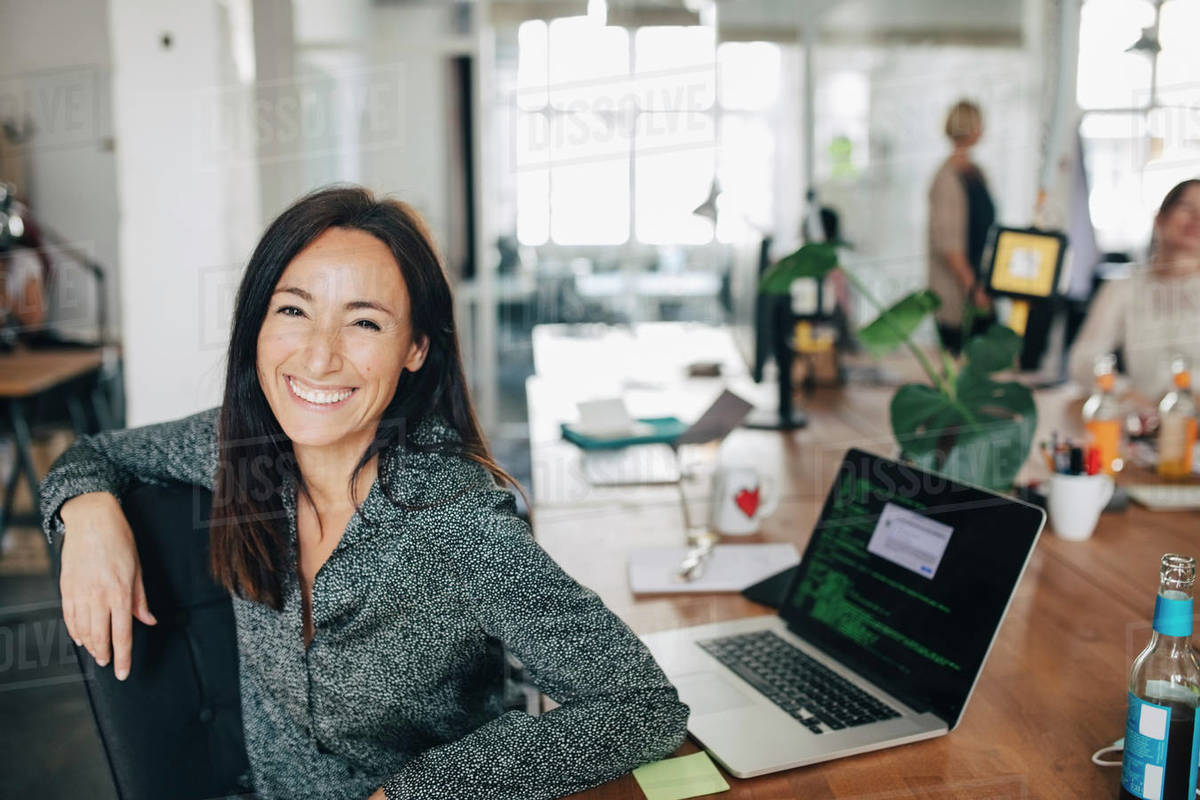 Portrait of smiling female computer programmer sitting at desk in ...