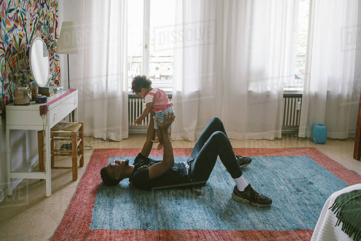Playful father lifting daughter while lying on carpet at home Stock