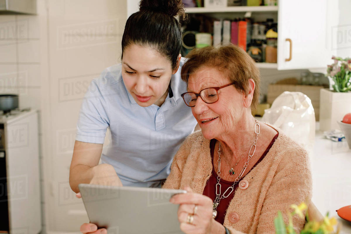Retired elderly woman looking while young female volunteer using