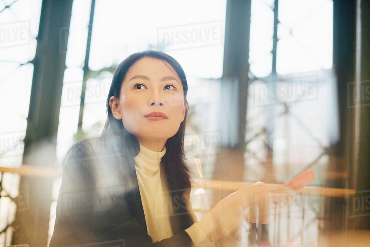 Confident businesswoman holding smart phone while looking away in office cafeteria Royalty-free stock photo