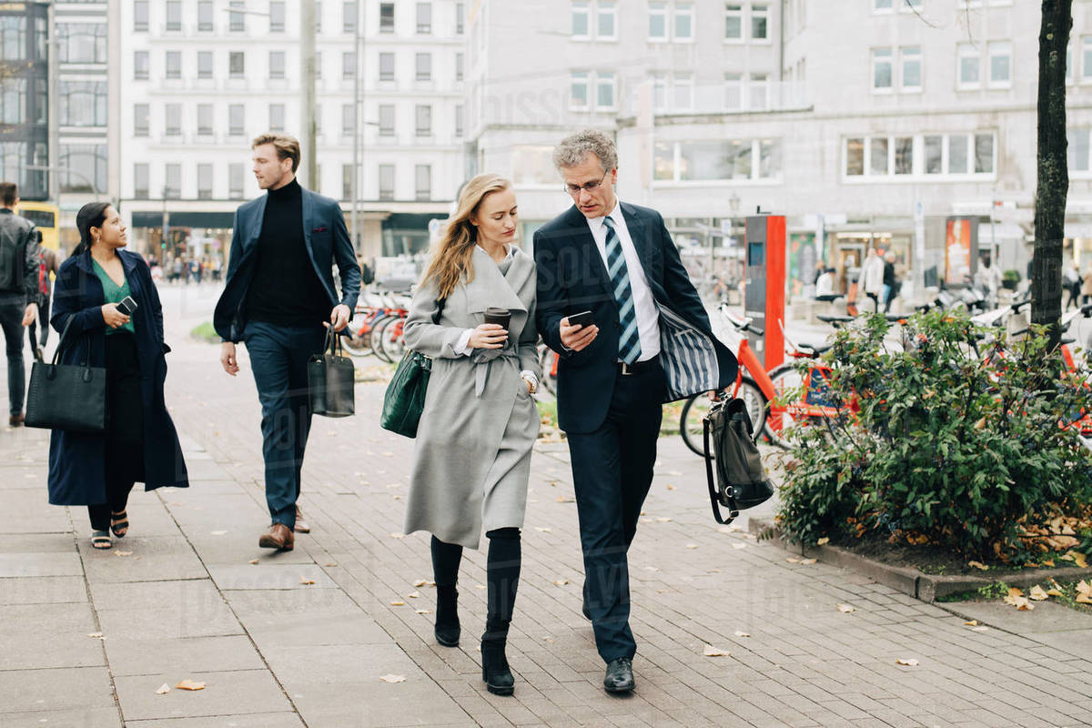 Businessman showing smart phone to female colleague while walking in city Royalty-free stock photo